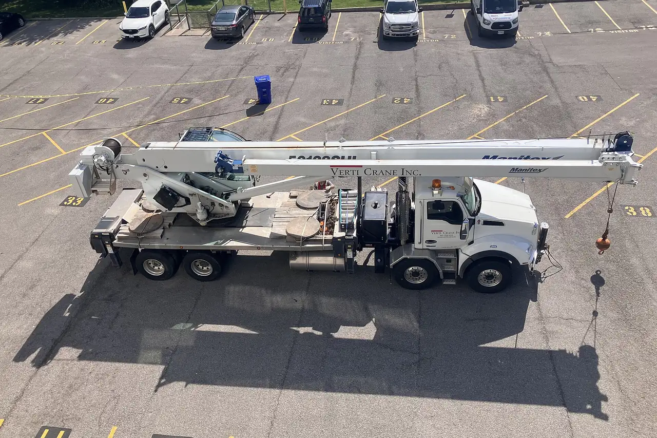 White truck-mounted telescopic boom crane parked in a lot with its boom stowed over the cab