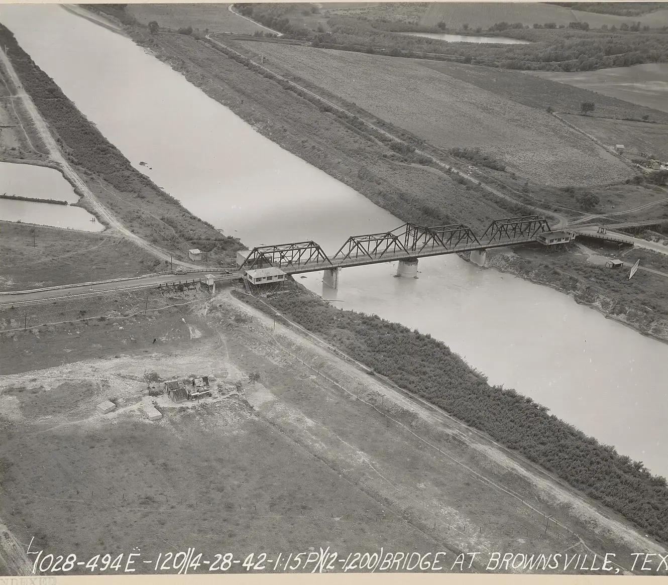 1942 aerial photograph of a steel truss bridge crossing the Rio Grande at Brownsville, with farm fields on both banks