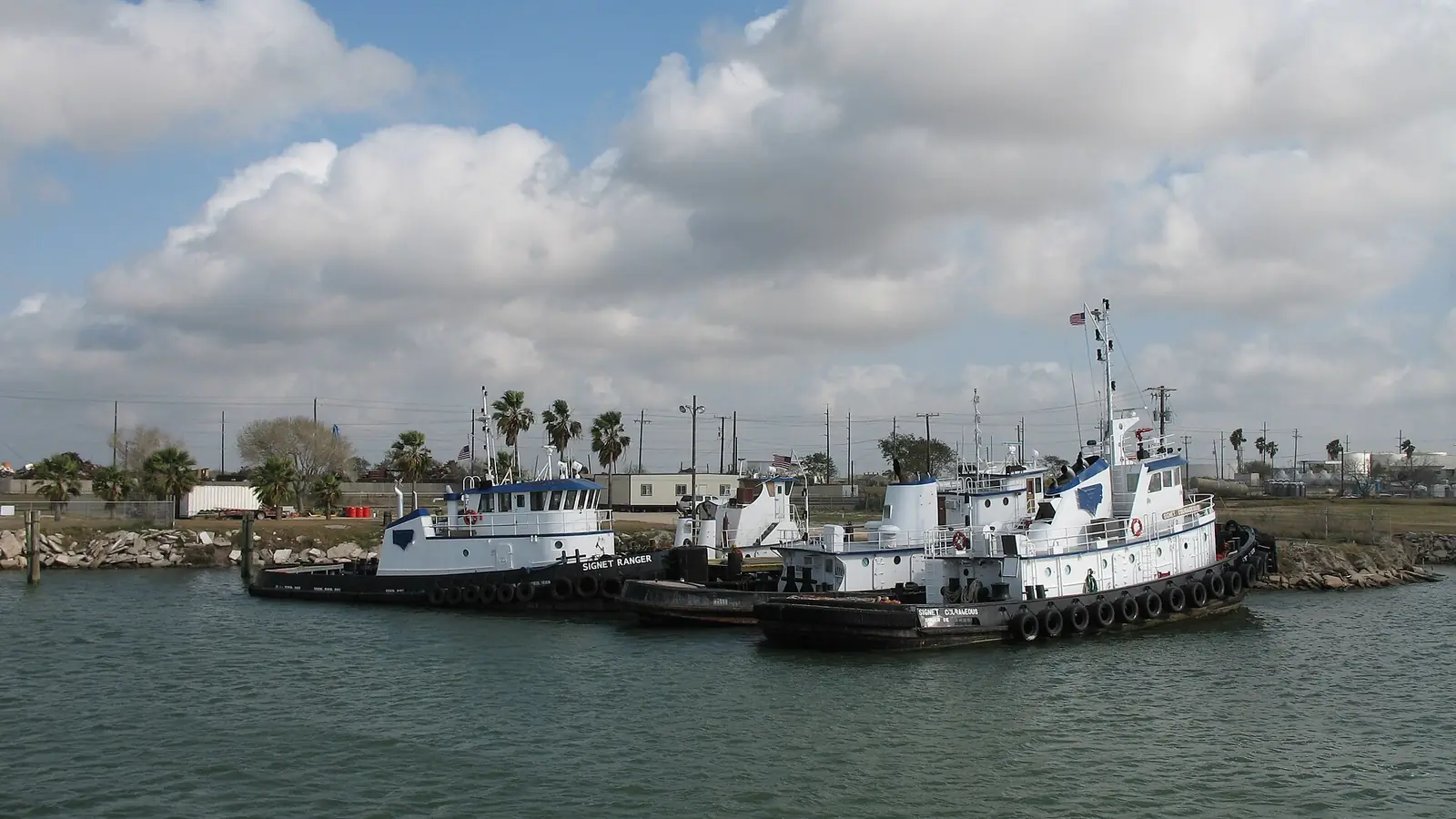 Tugboats moored at the Port of Brownsville under a wide sky, palm trees along the shore